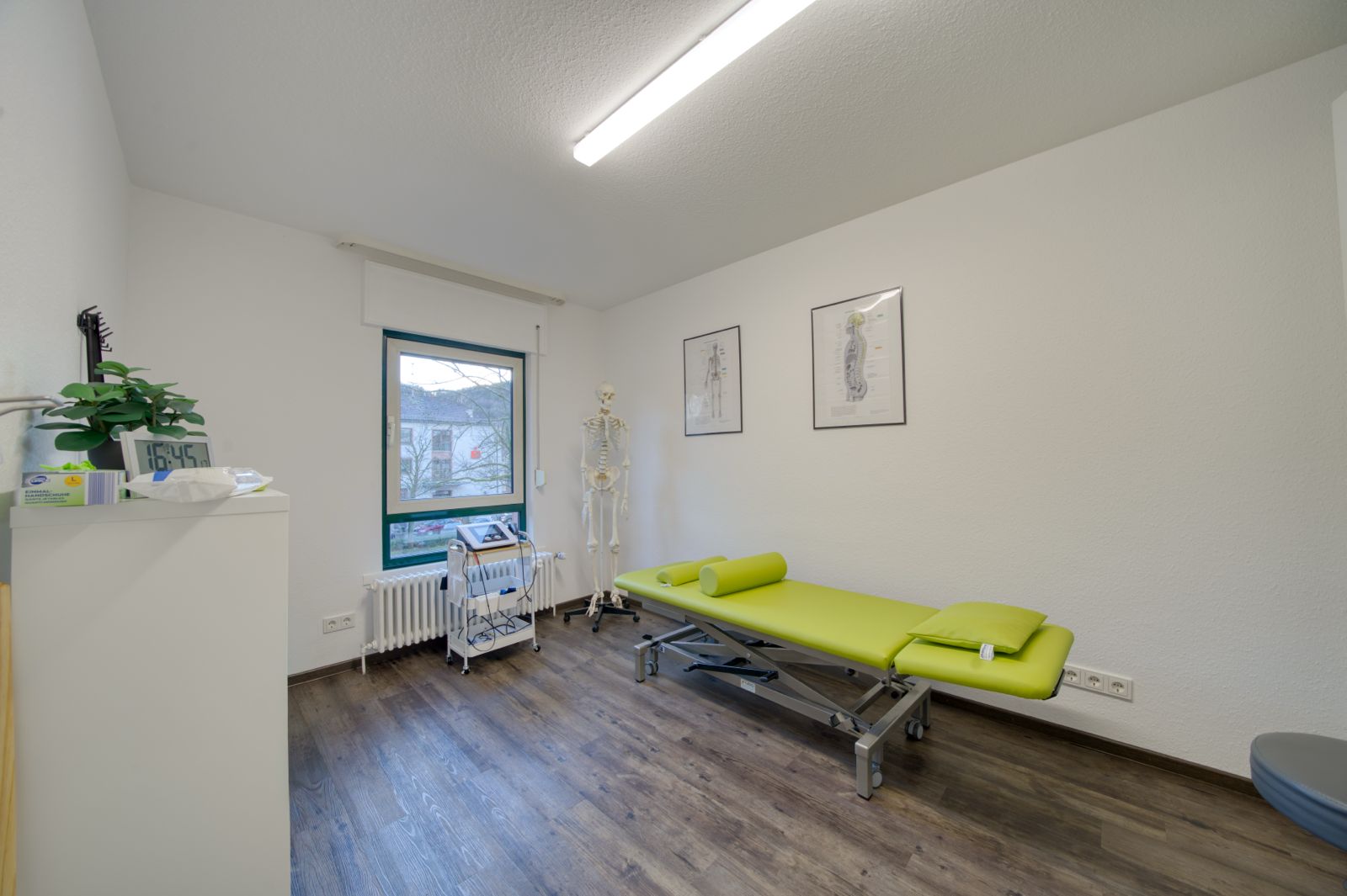 Ruhiger Behandlungsraum mit gruener Therapieliege